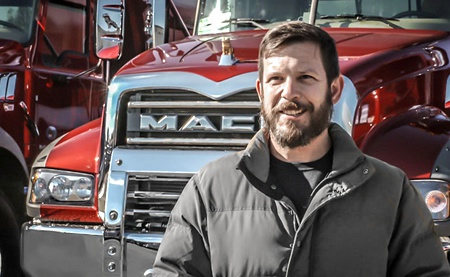 Image of a sales representative smiling standing in front of a Mack truck.